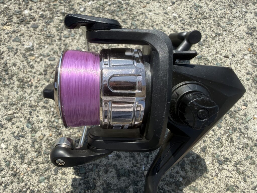 釣り入門時に使用していたダイソーのスピニングリール（パープルカラーのラインが巻かれている様子）